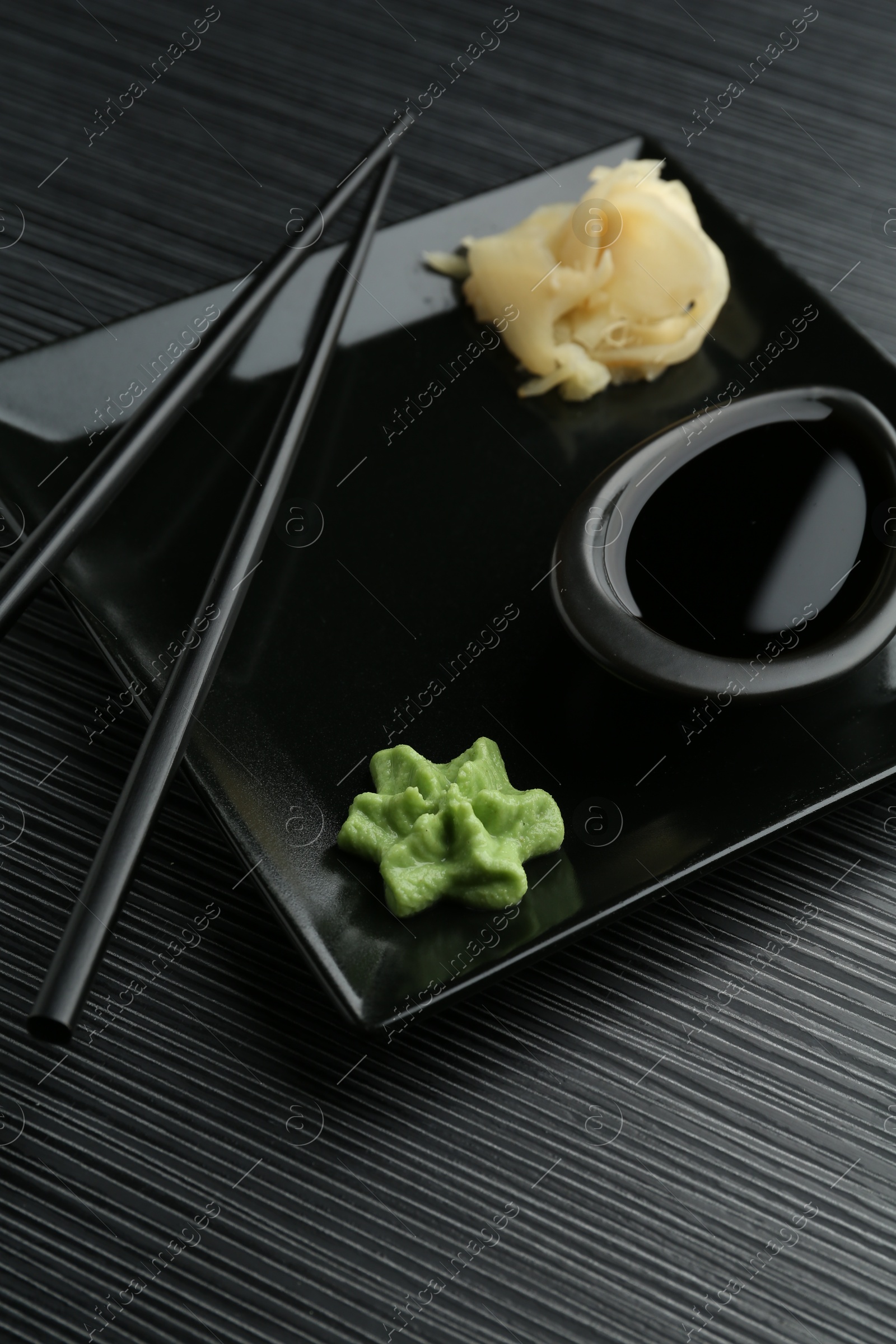 Photo of Hot wasabi paste, soy sauce, ginger and chopsticks on black textured table, closeup