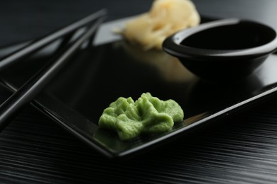 Photo of Hot wasabi paste, soy sauce, ginger and chopsticks on black textured table, closeup