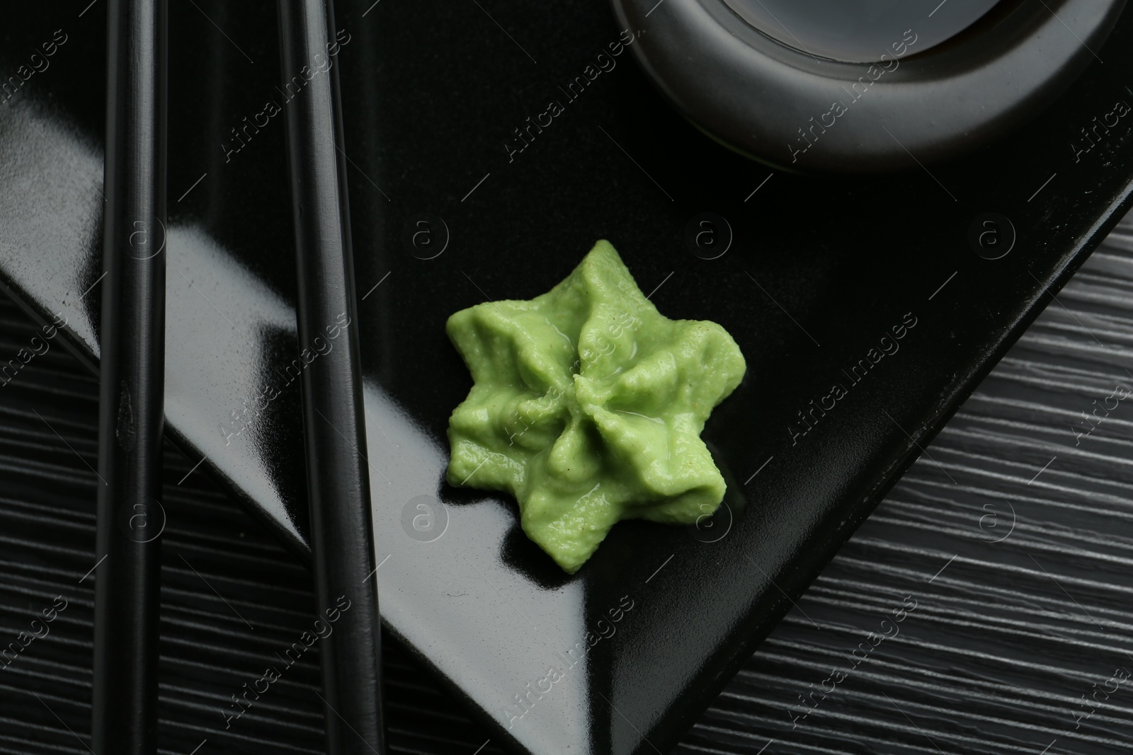 Photo of Hot wasabi paste and chopsticks on black textured table, top view