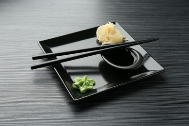 Photo of Hot wasabi paste, soy sauce, ginger and chopsticks on black textured table