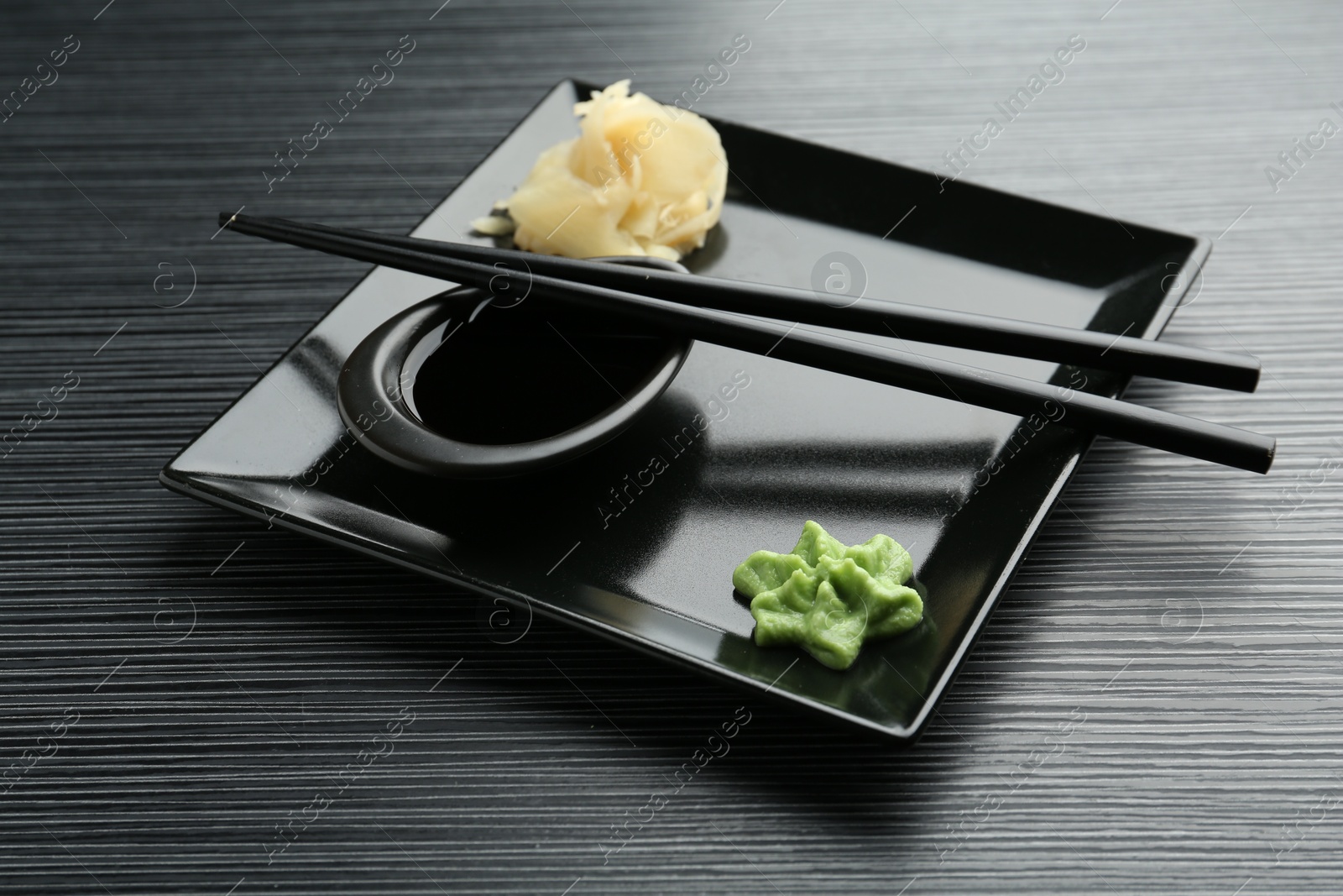 Photo of Hot wasabi paste, soy sauce, ginger and chopsticks on black textured table