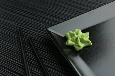 Photo of Plate with hot wasabi paste and chopsticks on black textured table, closeup