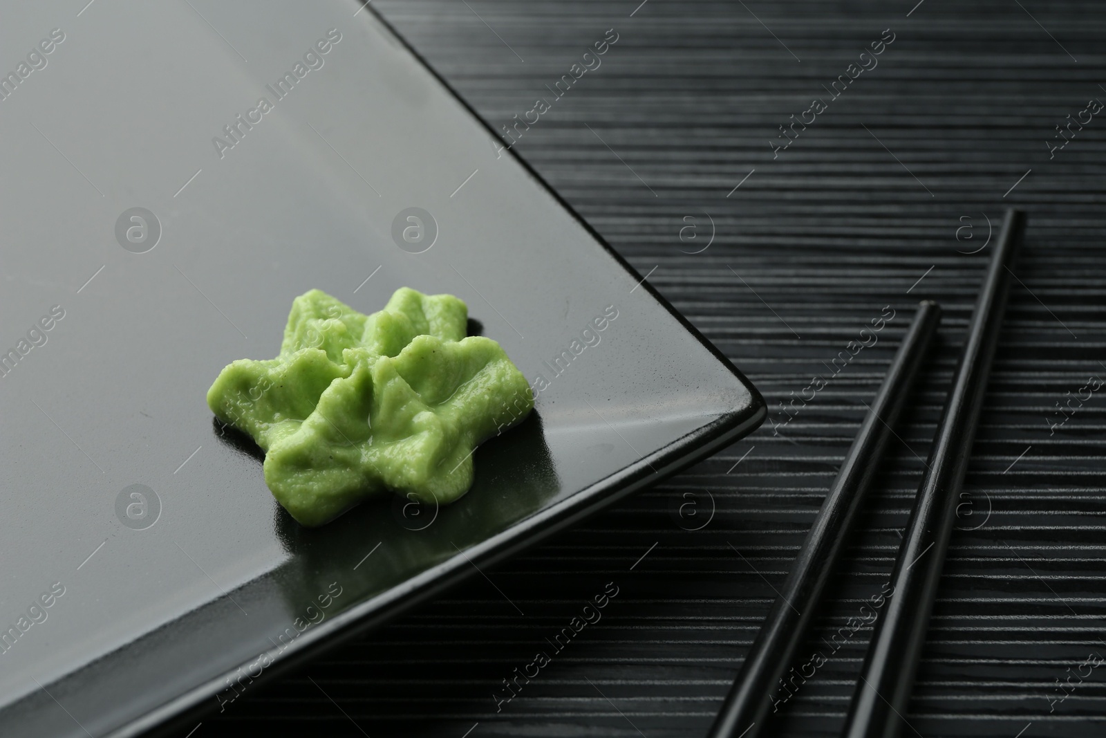 Photo of Plate with hot wasabi paste and chopsticks on black textured table, closeup