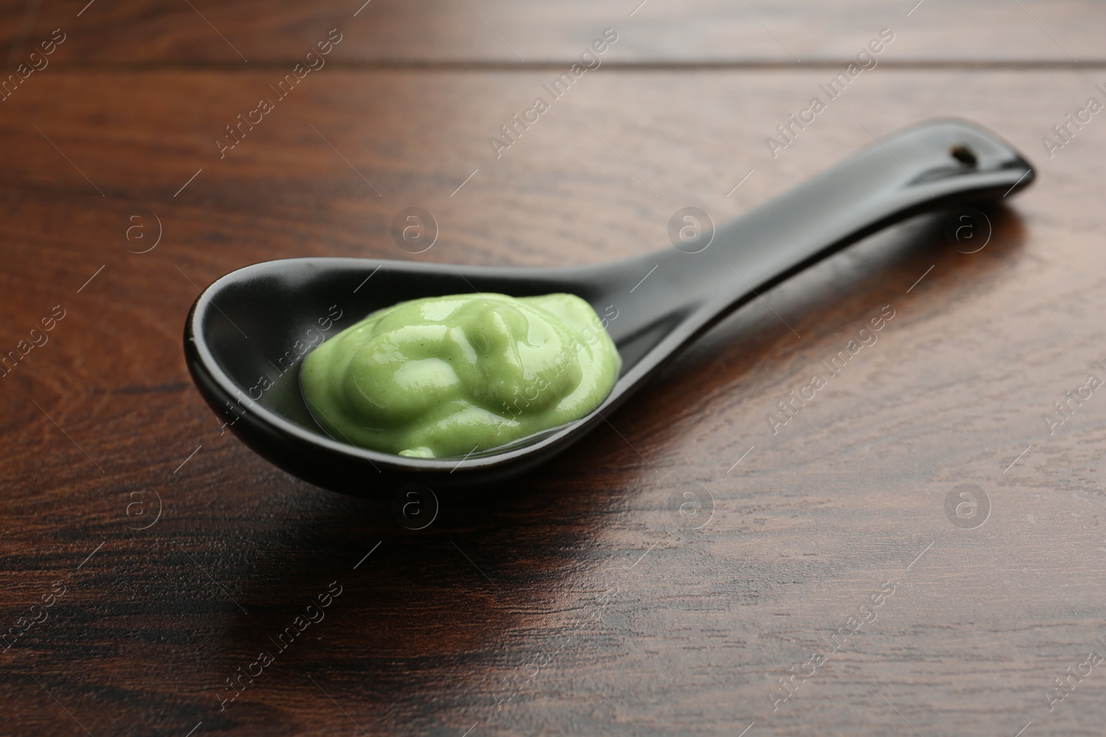 Photo of Spoon with hot wasabi paste on wooden table, closeup