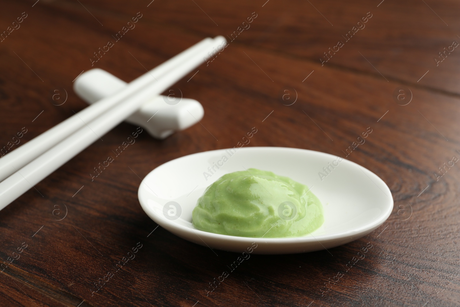 Photo of Hot wasabi paste and chopsticks on wooden table, closeup