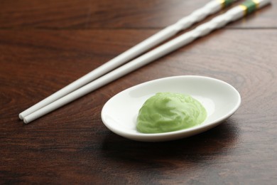 Photo of Hot wasabi paste and chopsticks on wooden table, closeup