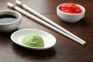 Photo of Hot wasabi paste, soy sauce, ginger and chopsticks on wooden table, closeup