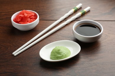 Photo of Hot wasabi paste, soy sauce, ginger and chopsticks on wooden table, closeup