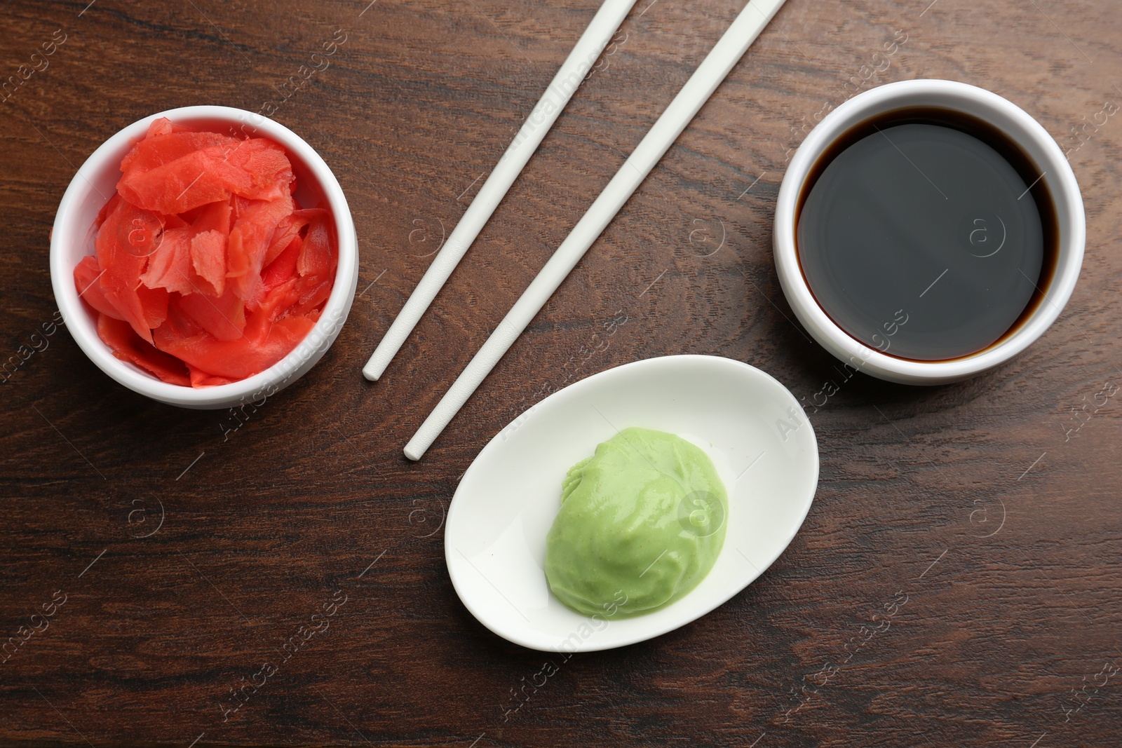 Photo of Hot wasabi paste, soy sauce, ginger and chopsticks on wooden table, flat lay