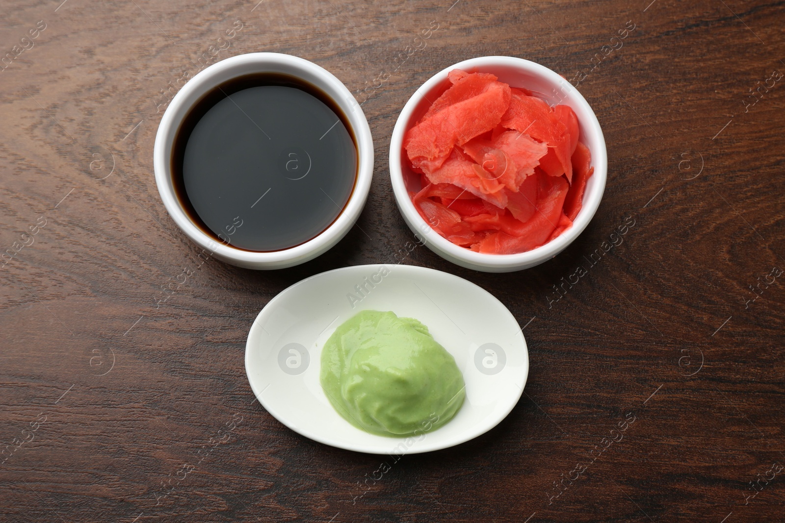 Photo of Hot wasabi paste, soy sauce and ginger on wooden table, flat lay