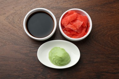 Photo of Hot wasabi paste, soy sauce and ginger on wooden table, flat lay