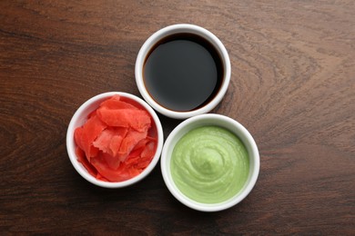 Photo of Hot wasabi paste, soy sauce and ginger on wooden table, flat lay