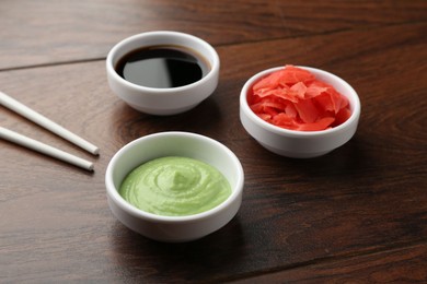 Photo of Hot wasabi paste, soy sauce, ginger and chopsticks on wooden table, closeup