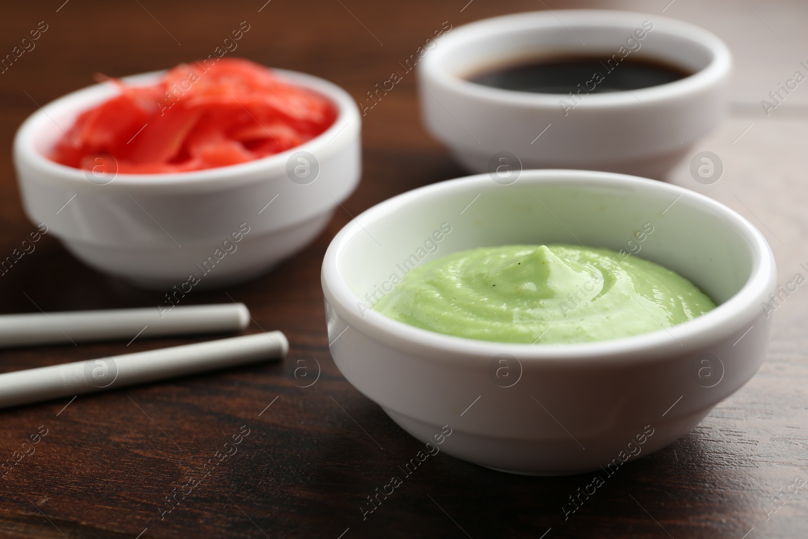 Photo of Hot wasabi paste, soy sauce, ginger and chopsticks on wooden table, closeup