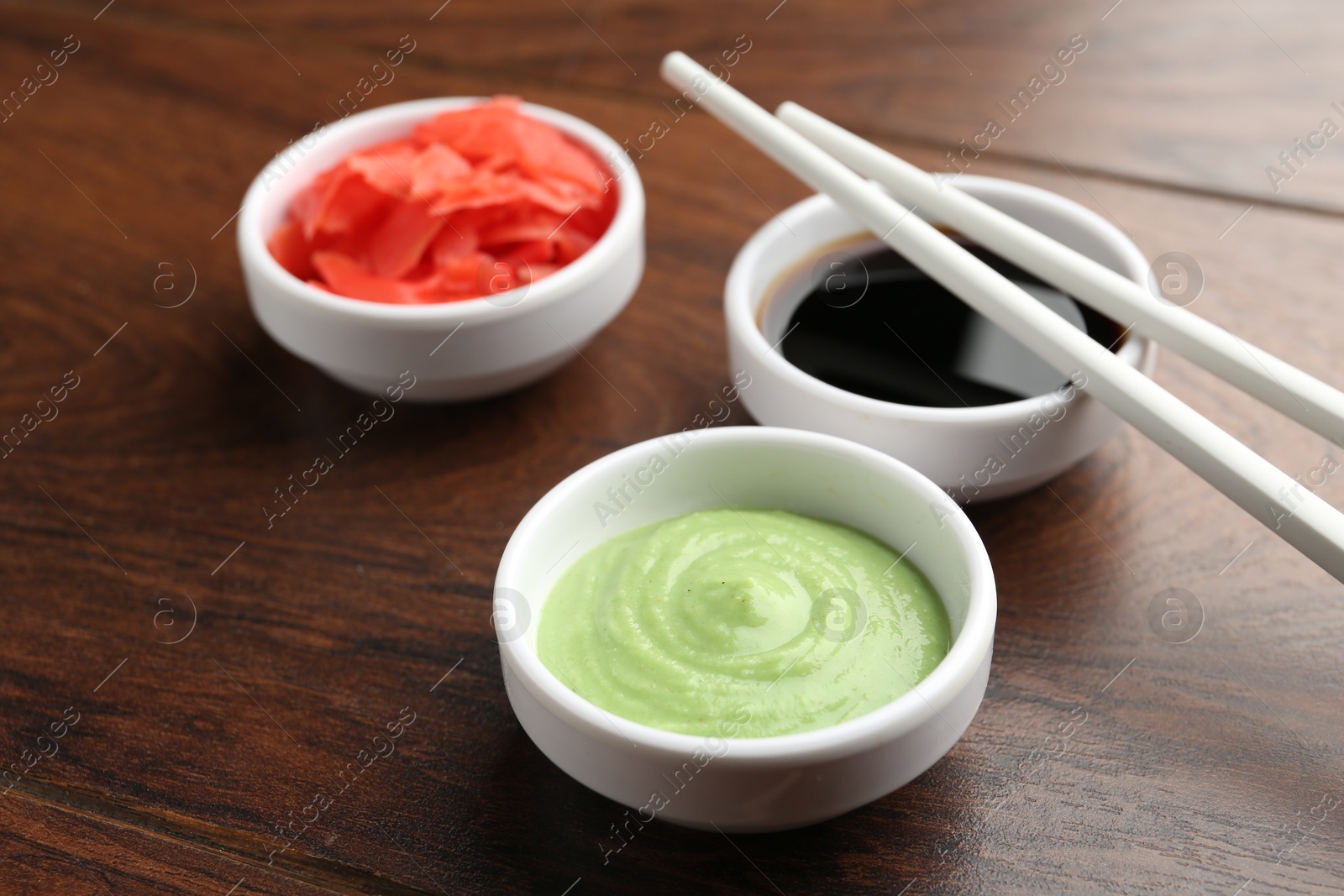 Photo of Hot wasabi paste, soy sauce, ginger and chopsticks on wooden table, closeup