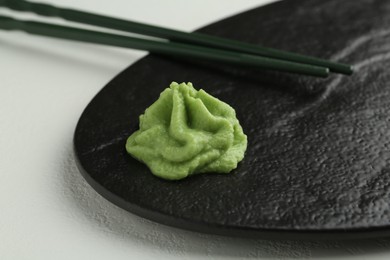 Photo of Slate board with hot wasabi paste and chopsticks on light textured table, closeup