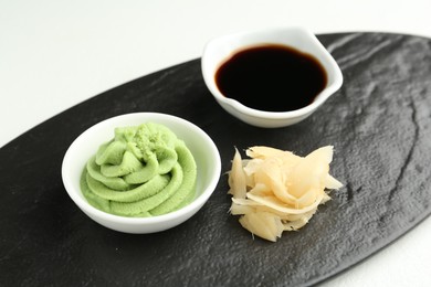 Photo of Slate board with hot wasabi paste, soy sauce and ginger on light textured table, closeup