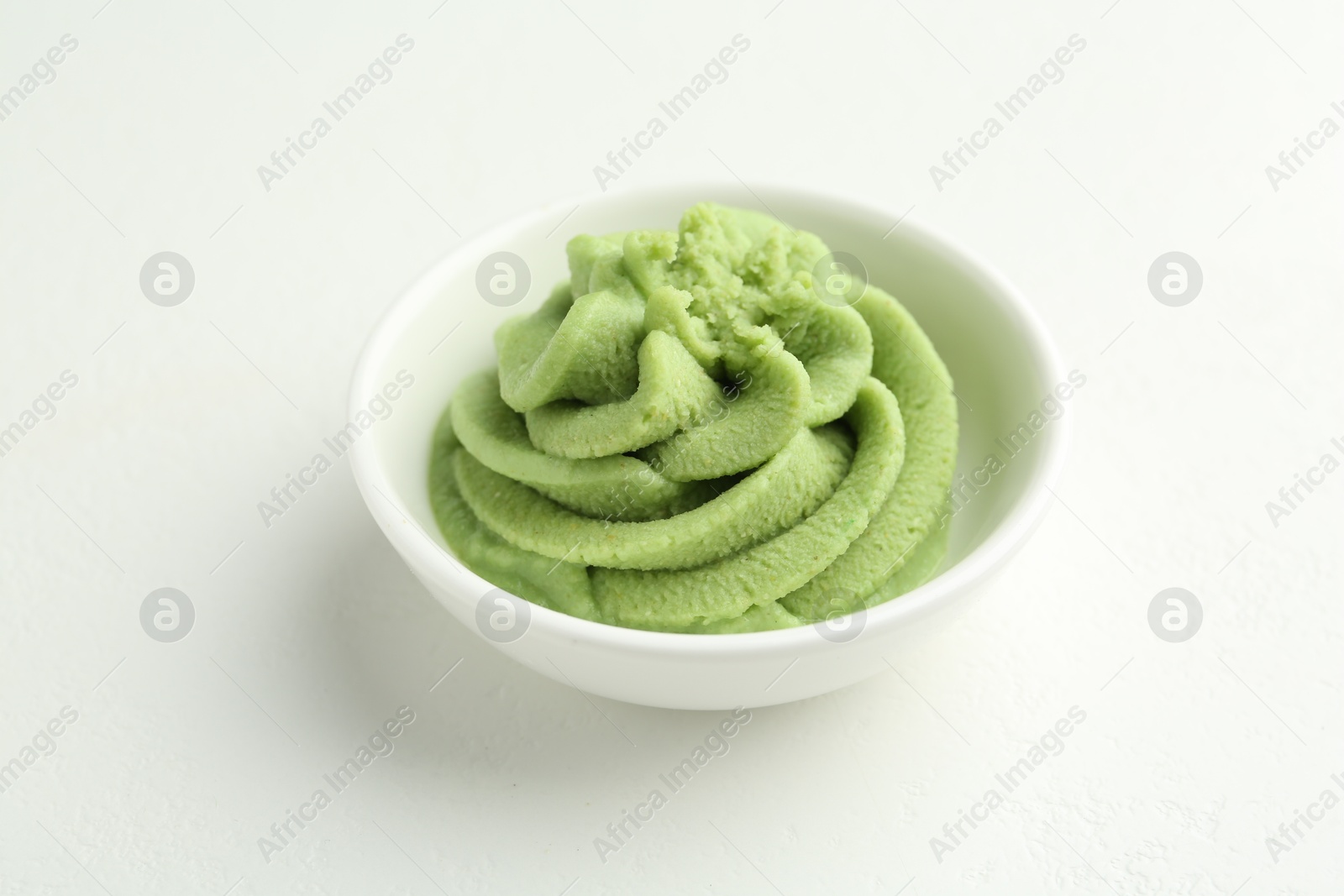 Photo of Hot wasabi paste in bowl on light textured table, closeup