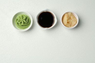 Photo of Hot wasabi paste, soy sauce and ginger on light textured table, flat lay. Space for text