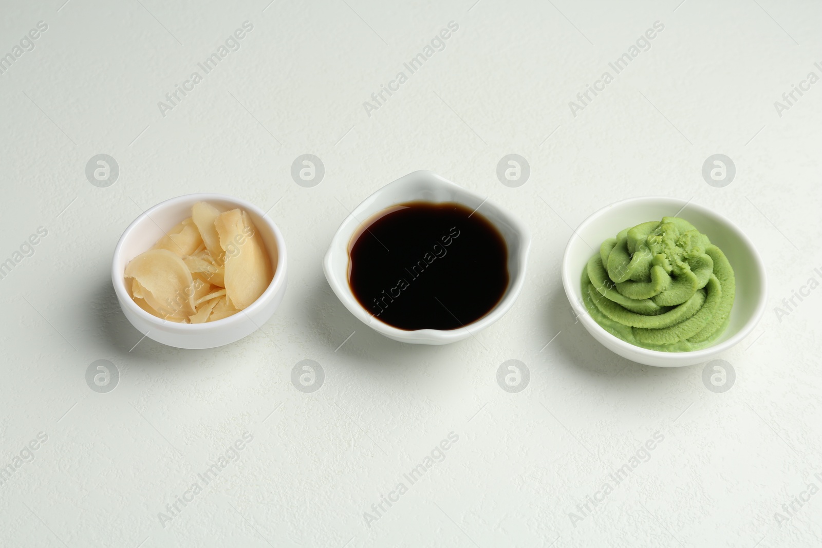 Photo of Hot wasabi paste, soy sauce and ginger on light textured table