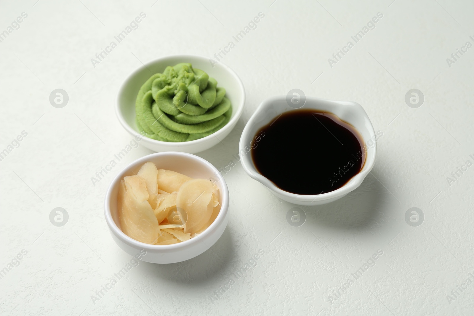 Photo of Hot wasabi paste, soy sauce and ginger on light textured table, closeup