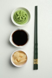 Photo of Hot wasabi paste, soy sauce, ginger and chopsticks on light textured table, flat lay