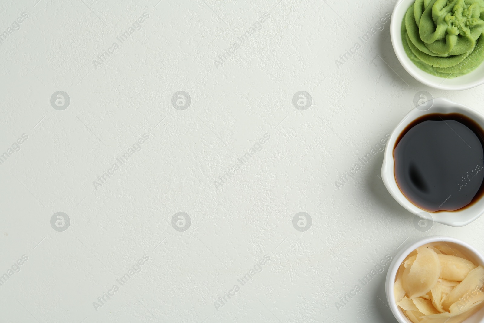 Photo of Hot wasabi paste, soy sauce and ginger on light textured table, flat lay. Space for text