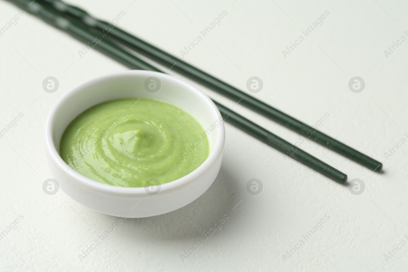 Photo of Hot wasabi paste in bowl and chopsticks on light textured table, closeup