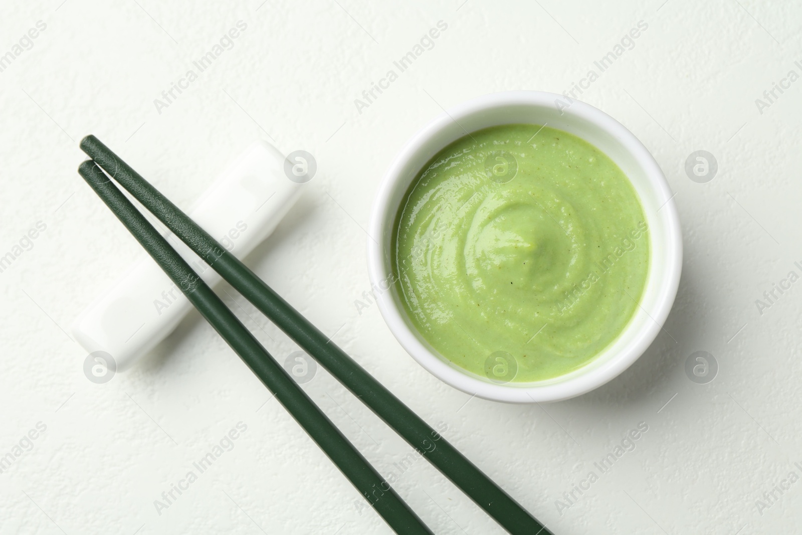 Photo of Hot wasabi paste in bowl and chopsticks on light textured table, top view