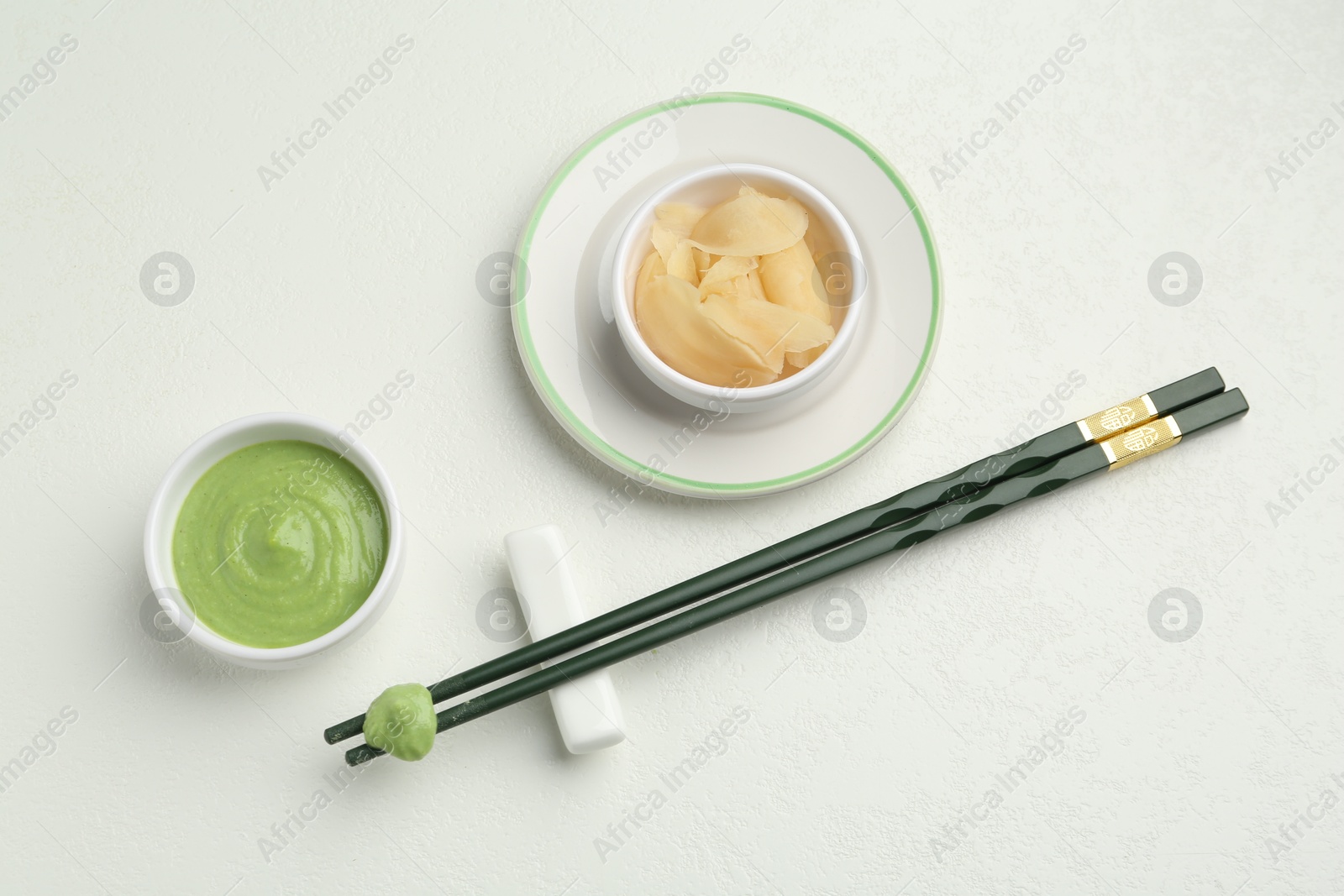 Photo of Hot wasabi paste, ginger and chopsticks on light textured table, flat lay