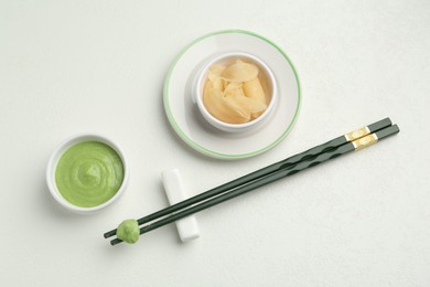 Photo of Hot wasabi paste, ginger and chopsticks on light textured table, flat lay