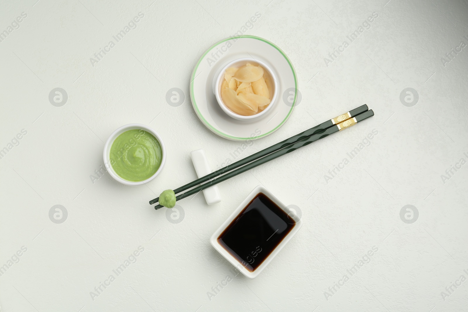 Photo of Hot wasabi paste, ginger, soy sauce and chopsticks on light textured table, flat lay