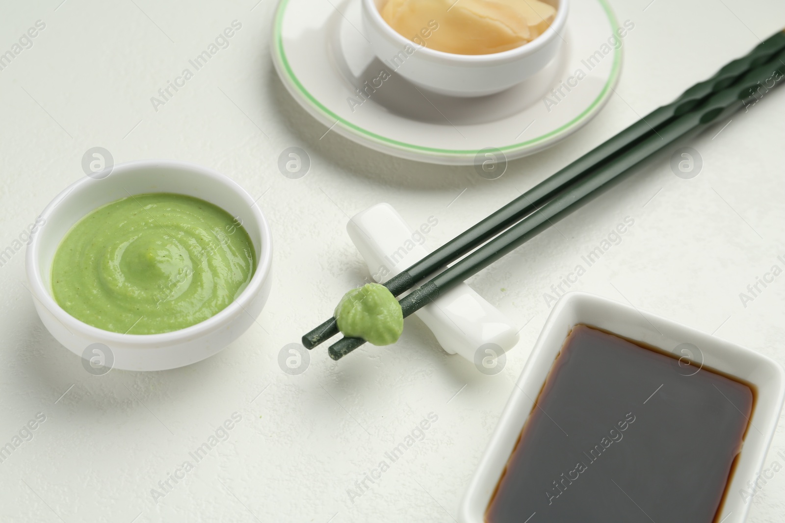 Photo of Hot wasabi paste, ginger, soy sauce and chopsticks on light textured table, closeup