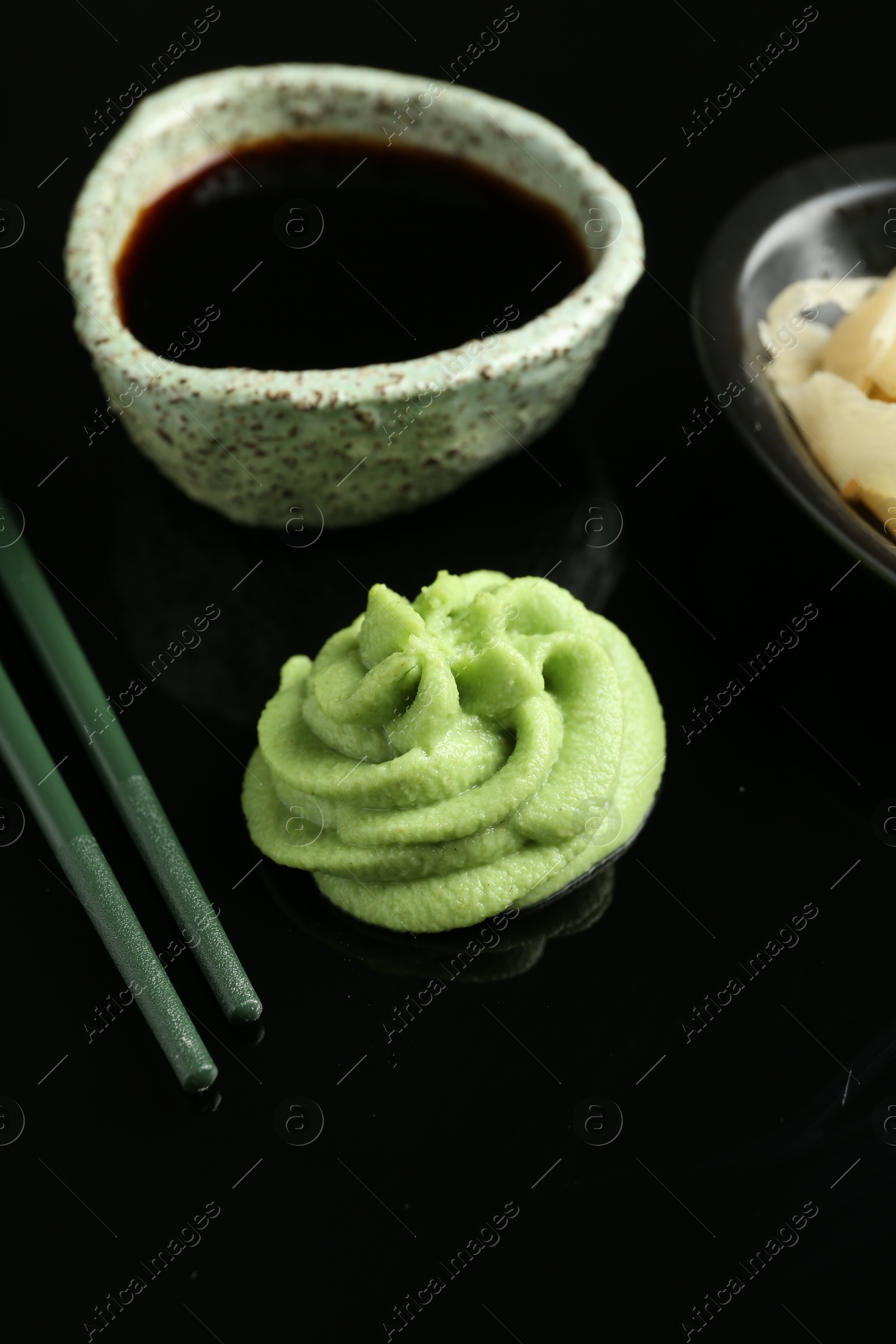 Photo of Hot wasabi paste, soy sauce and chopsticks on black mirror surface