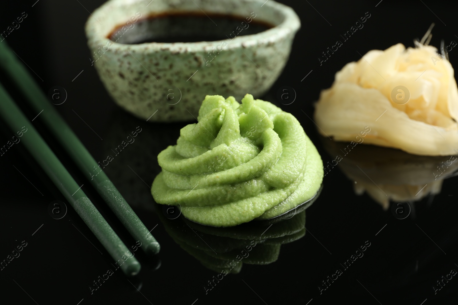 Photo of Hot wasabi paste, soy sauce, ginger and chopsticks on black mirror surface, closeup