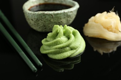 Photo of Hot wasabi paste, soy sauce, ginger and chopsticks on black mirror surface, closeup