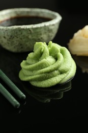 Photo of Hot wasabi paste, soy sauce and chopsticks on black mirror surface, closeup