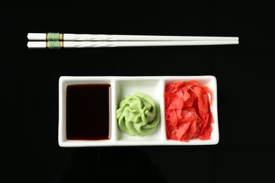 Photo of Hot wasabi paste, soy sauce, ginger and chopsticks on black background, flat lay