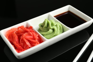 Photo of Hot wasabi paste, soy sauce and ginger on black mirror surface, closeup