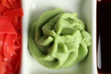 Photo of Hot wasabi paste, soy sauce and ginger on plate, top view