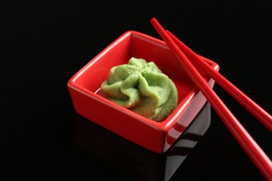 Photo of Hot wasabi paste in bowl and chopsticks on black mirror surface, closeup