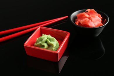 Photo of Hot wasabi paste, ginger and chopsticks on black mirror surface, closeup