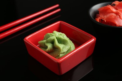 Photo of Hot wasabi paste, ginger and chopsticks on black mirror surface, closeup