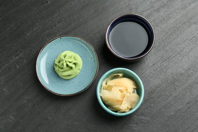 Photo of Hot wasabi paste, soy sauce and ginger on dark textured table, flat lay