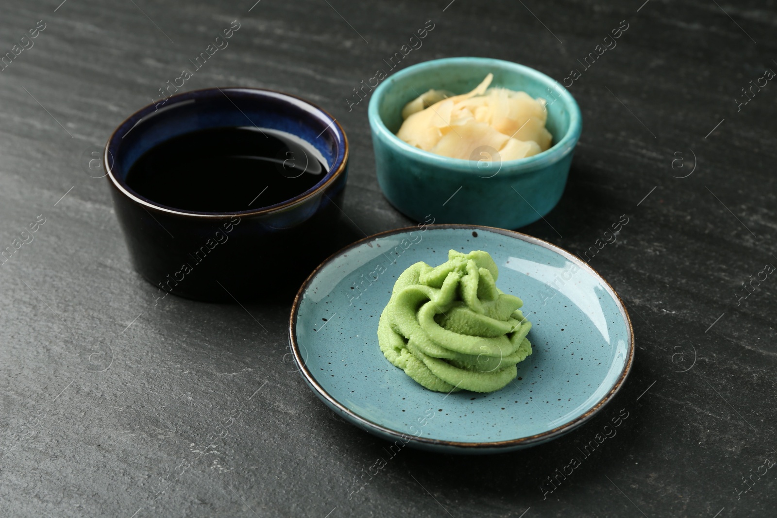 Photo of Hot wasabi paste, soy sauce and ginger on dark textured table, closeup