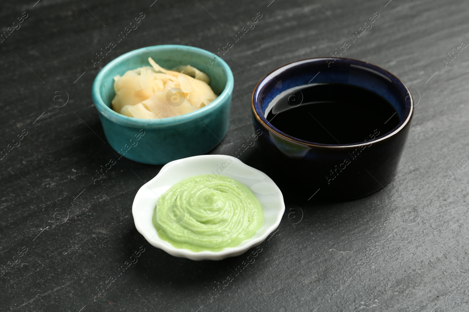 Photo of Hot wasabi paste, soy sauce and ginger on dark textured table, closeup