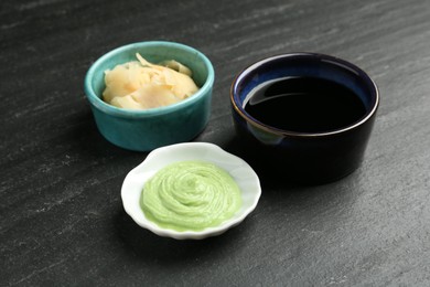 Photo of Hot wasabi paste, soy sauce and ginger on dark textured table, closeup