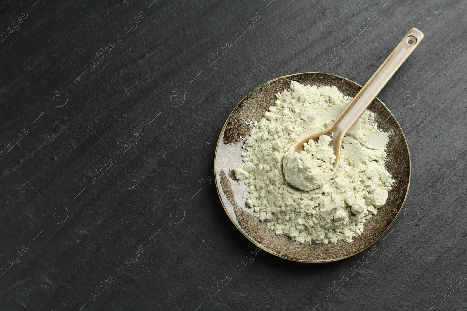 Photo of Plate with dry wasabi powder and spoon on dark textured table, top view. Space for text