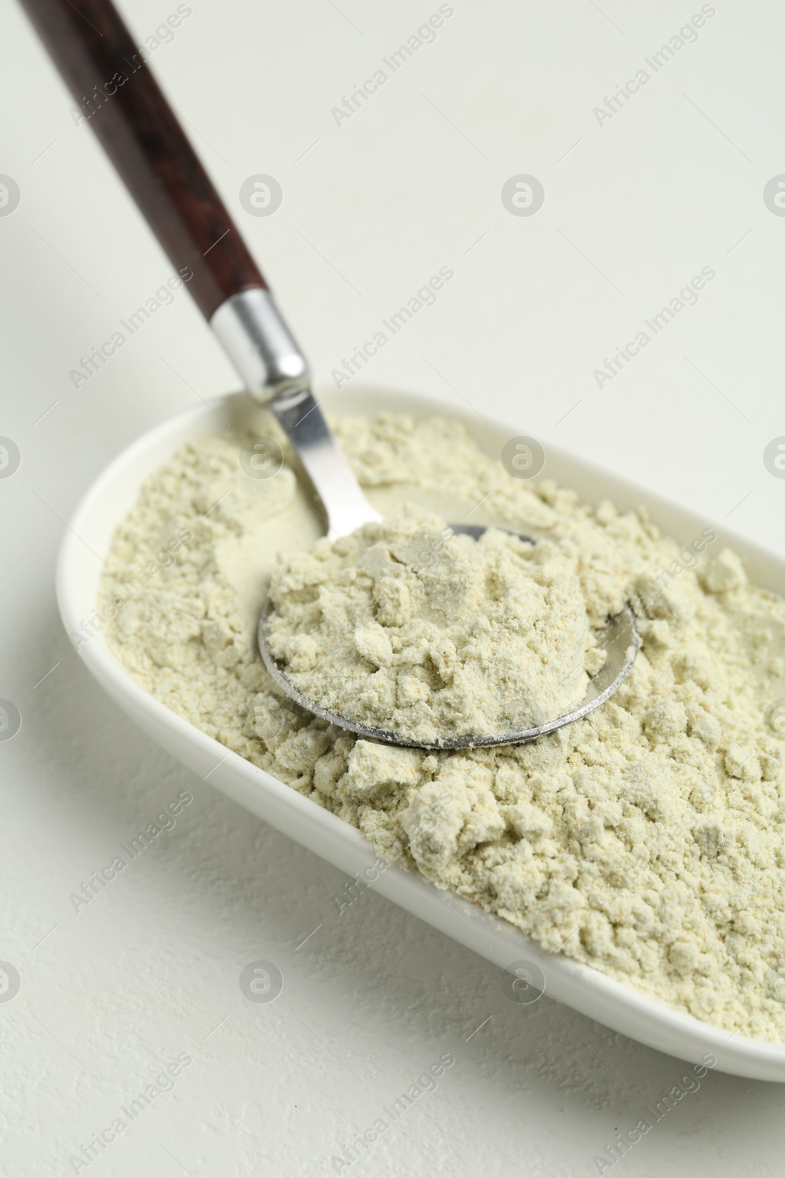 Photo of Dry wasabi powder and spoon on white textured table, closeup