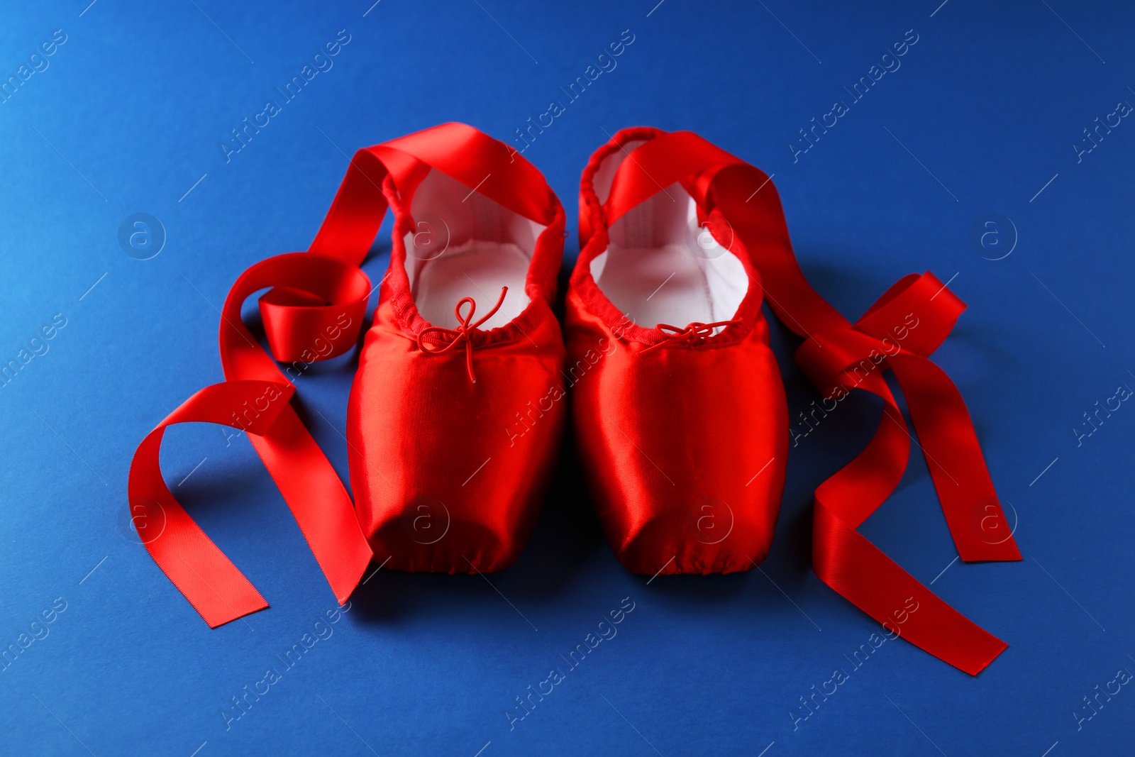 Photo of Pair of beautiful red pointe shoes on blue background